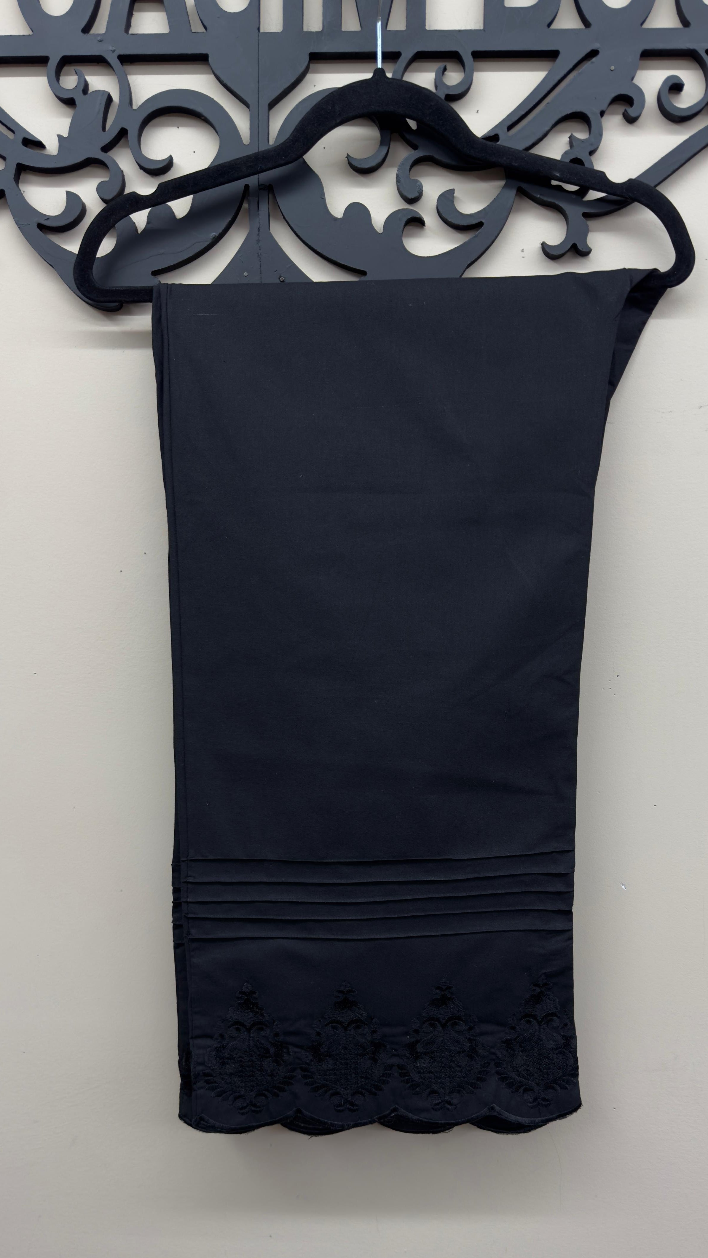 horizontal pin-tuck pleats and scalloped embroidery pattern on black cotton pants.