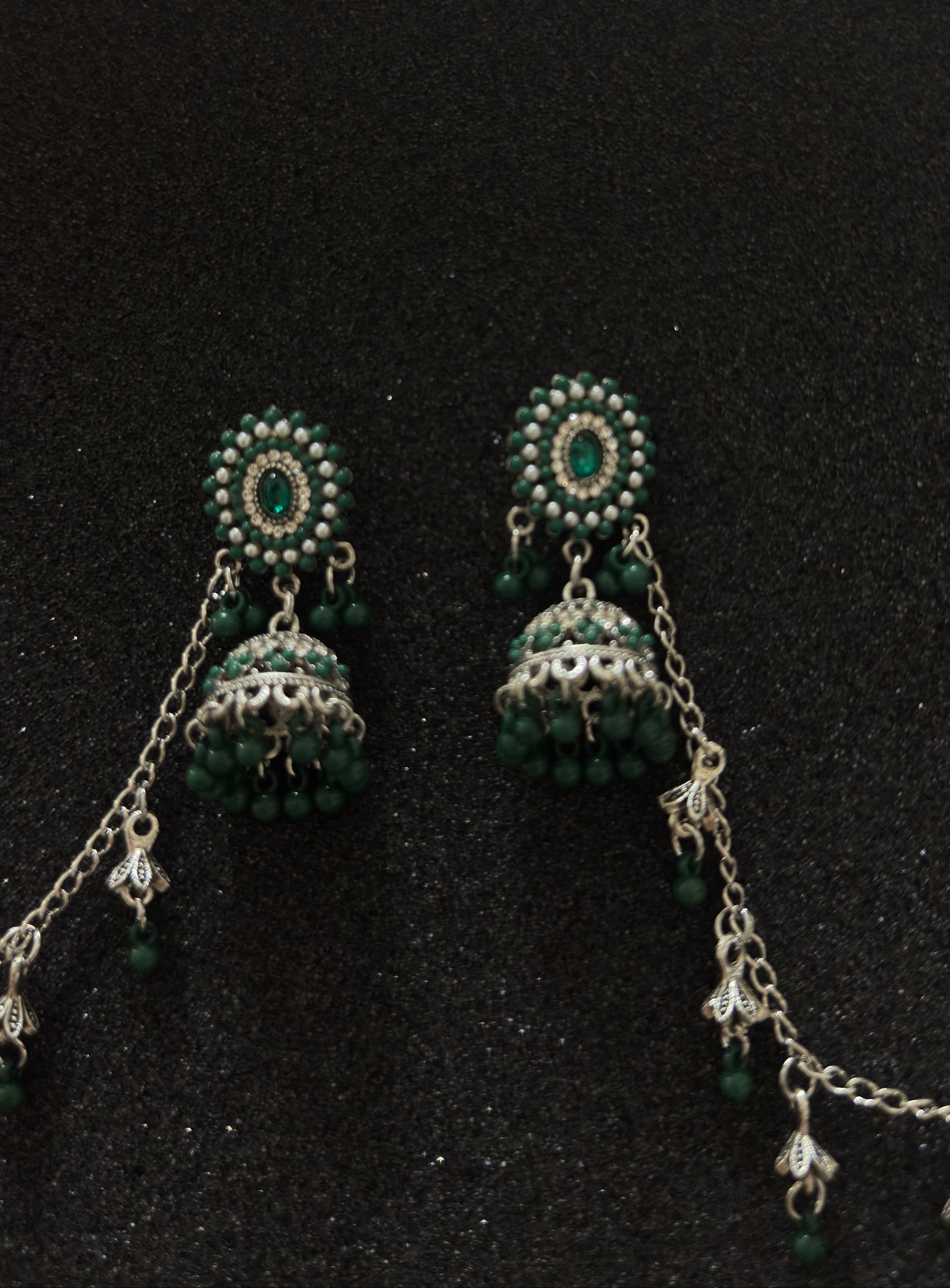 Oxidized silver jhumka earrings with emerald green stones and decorative sahara chain.