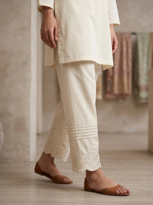 horizontal pin-tuck pleats and scalloped motif embroidery on off-white cotton pants.