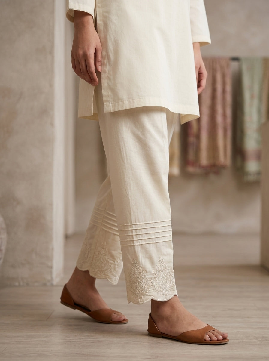horizontal pin-tuck pleats and scalloped motif embroidery on off-white cotton pants.