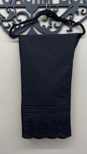 horizontal pin-tuck pleats and scalloped embroidery pattern on black cotton pants.